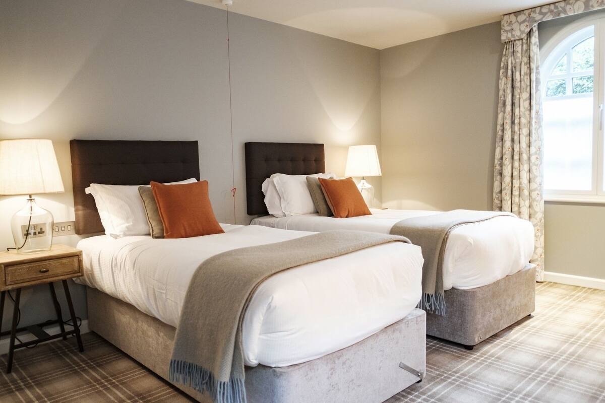 Ein Hotelzimmer mit zwei Betten, jeweils mit Kopfteil, Nachttisch und Lampe.