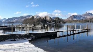 A wooden pier extending into a calm lake with snow on the ground, surrounded by mountains and trees.