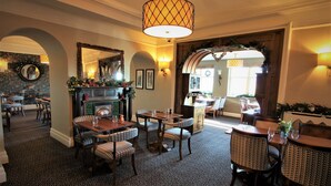 A cozy dining area with patterned chairs and tables, a fireplace with festive decorations, and a large mirror above the mantel. - Ravenstone Manor (Keswick)