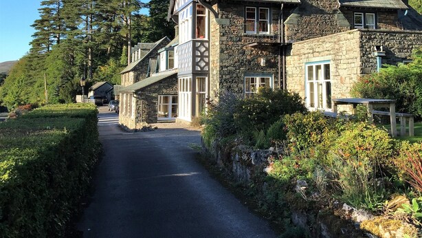 A stone building with a steeply pitched roof, multiple chimneys, and a small balcony. - Ravenstone Manor (Keswick)
