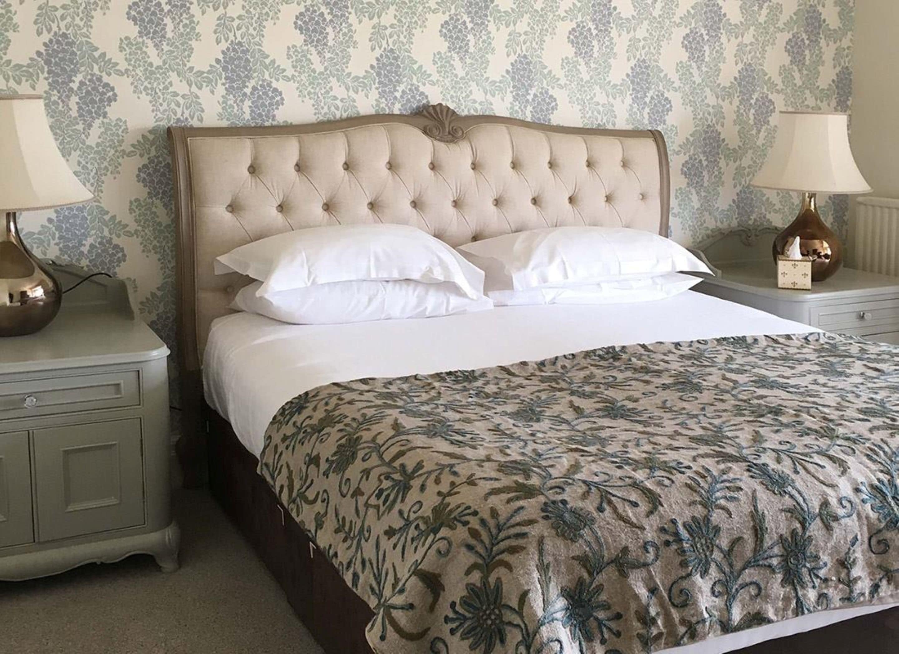 A neatly made bed with a floral bedspread, two bedside lamps, and a nightstand with a drawer.