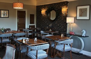 A dining area with patterned chairs, wooden tables, and a decorative mirror on the wall.