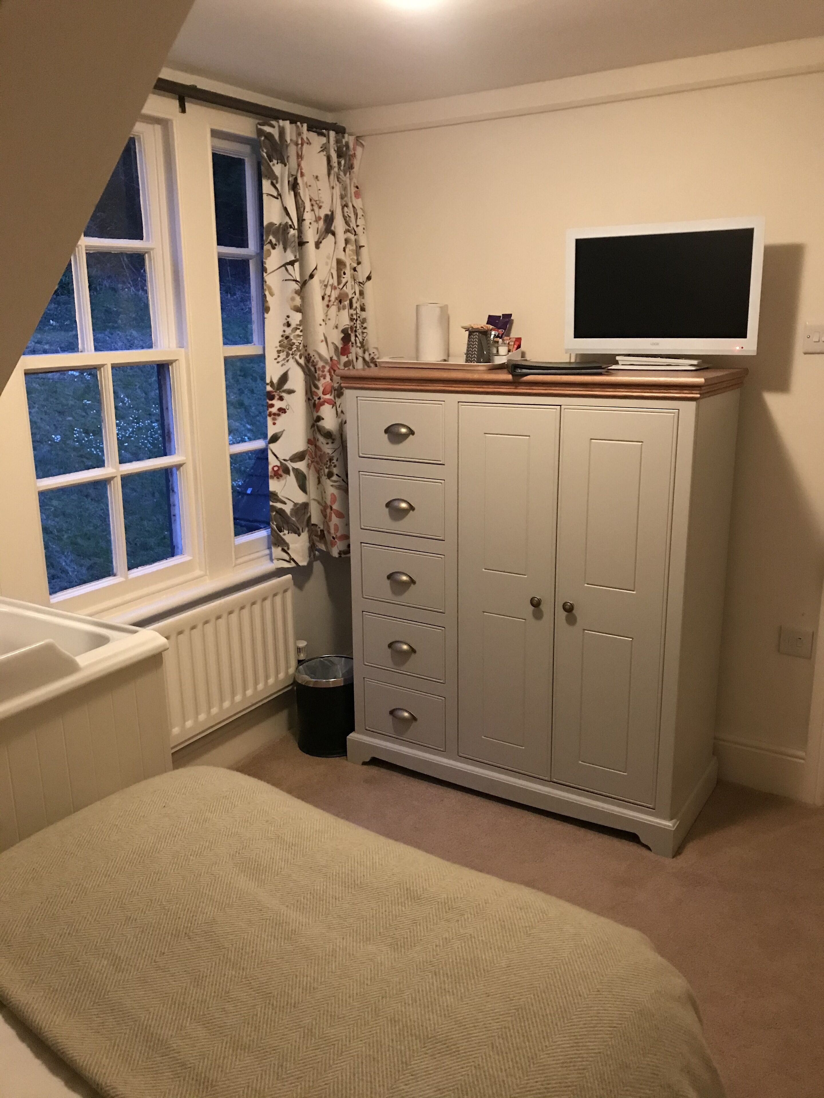 A bedroom with a bed, a wardrobe, a radiator, a window, and a television.