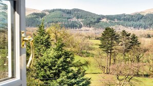 A view from inside a room with a window overlooking a landscape with hills, trees, and a body of water. - Ravenstone Manor (Keswick)