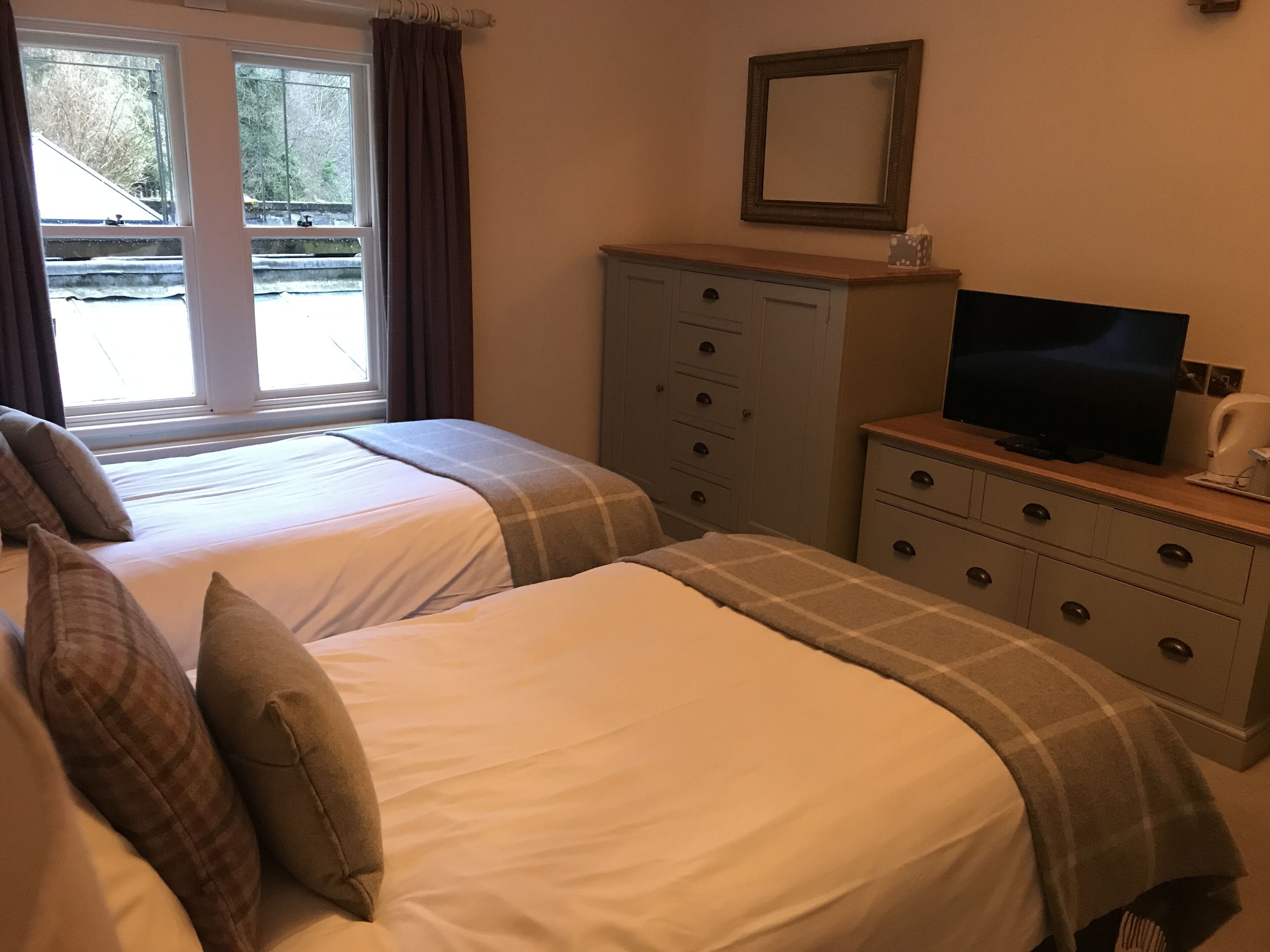 A hotel room with two beds, a dresser with a television, and a window with curtains.