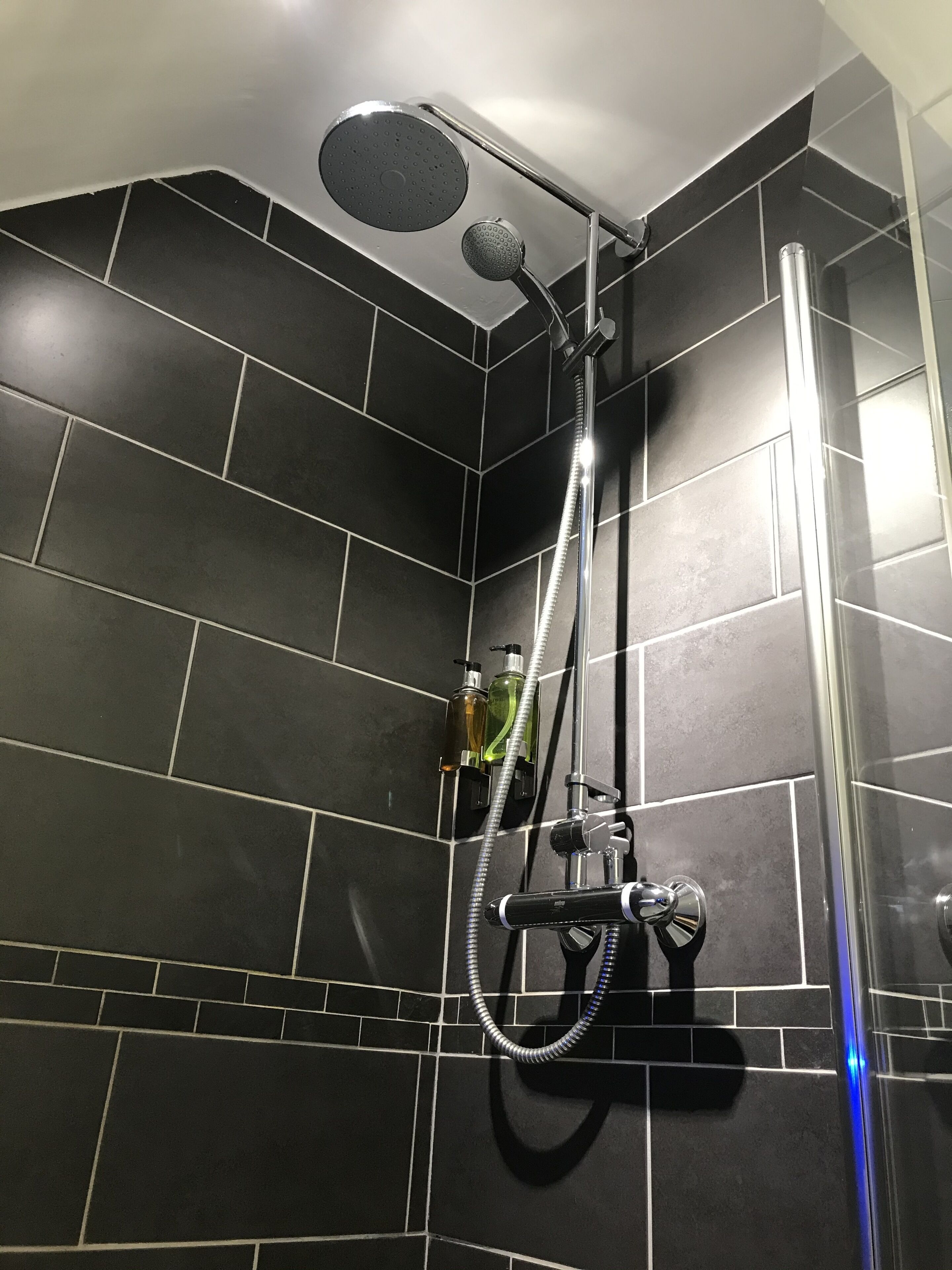 A shower with a handheld showerhead, a wall-mounted showerhead, and a handheld massage nozzle.