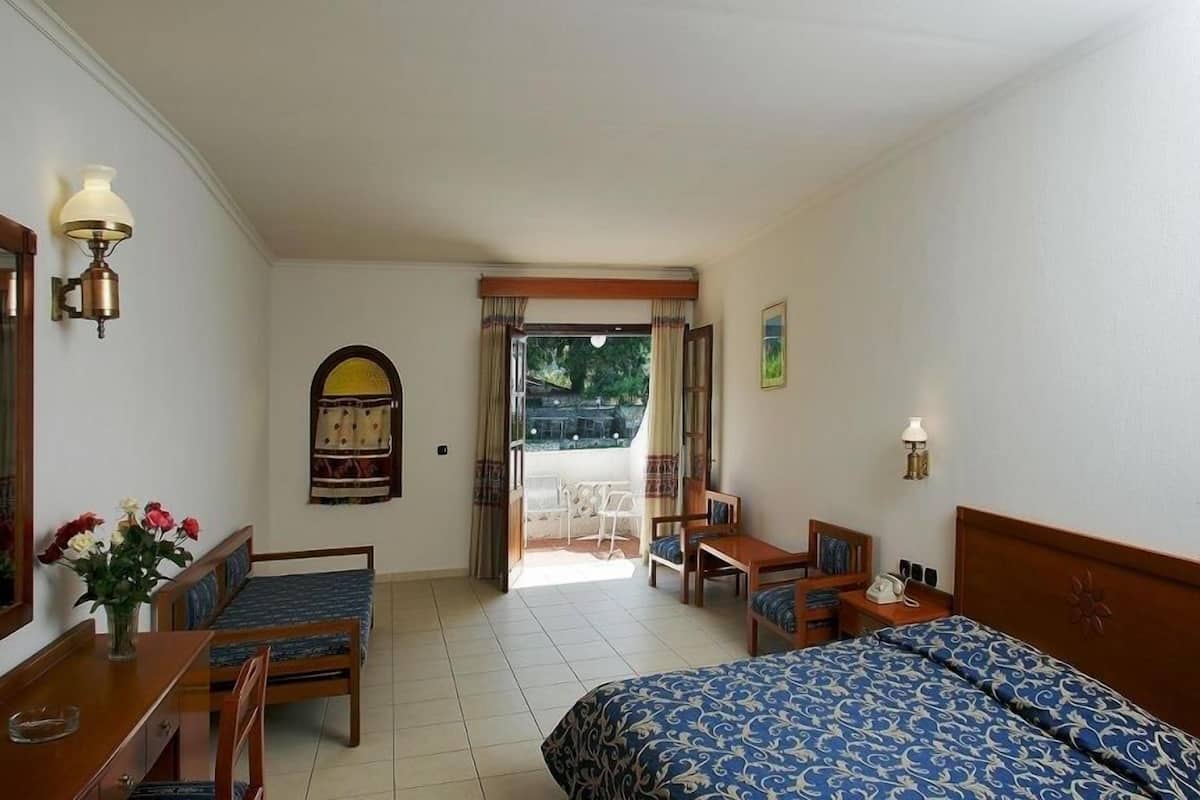 A hotel room with a bed, a desk, a chair, a small table, a mirror, and a window with curtains.