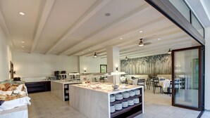A modern kitchen with a marble island, dining area with chairs, and a large window. - GHotels Macedonian Sun (Kassandra)