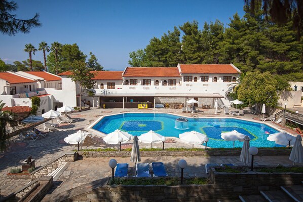 A swimming pool surrounded by lounge chairs and umbrellas, with a building in the background. - GHotels Macedonian Sun (Kassandra)