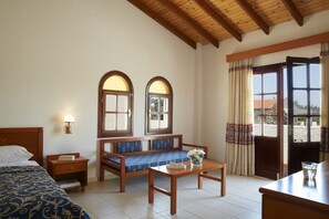 Habitació d'hotel amb llit, una panxa de fusta amb coixins, taula petita i finestra amb cortines.