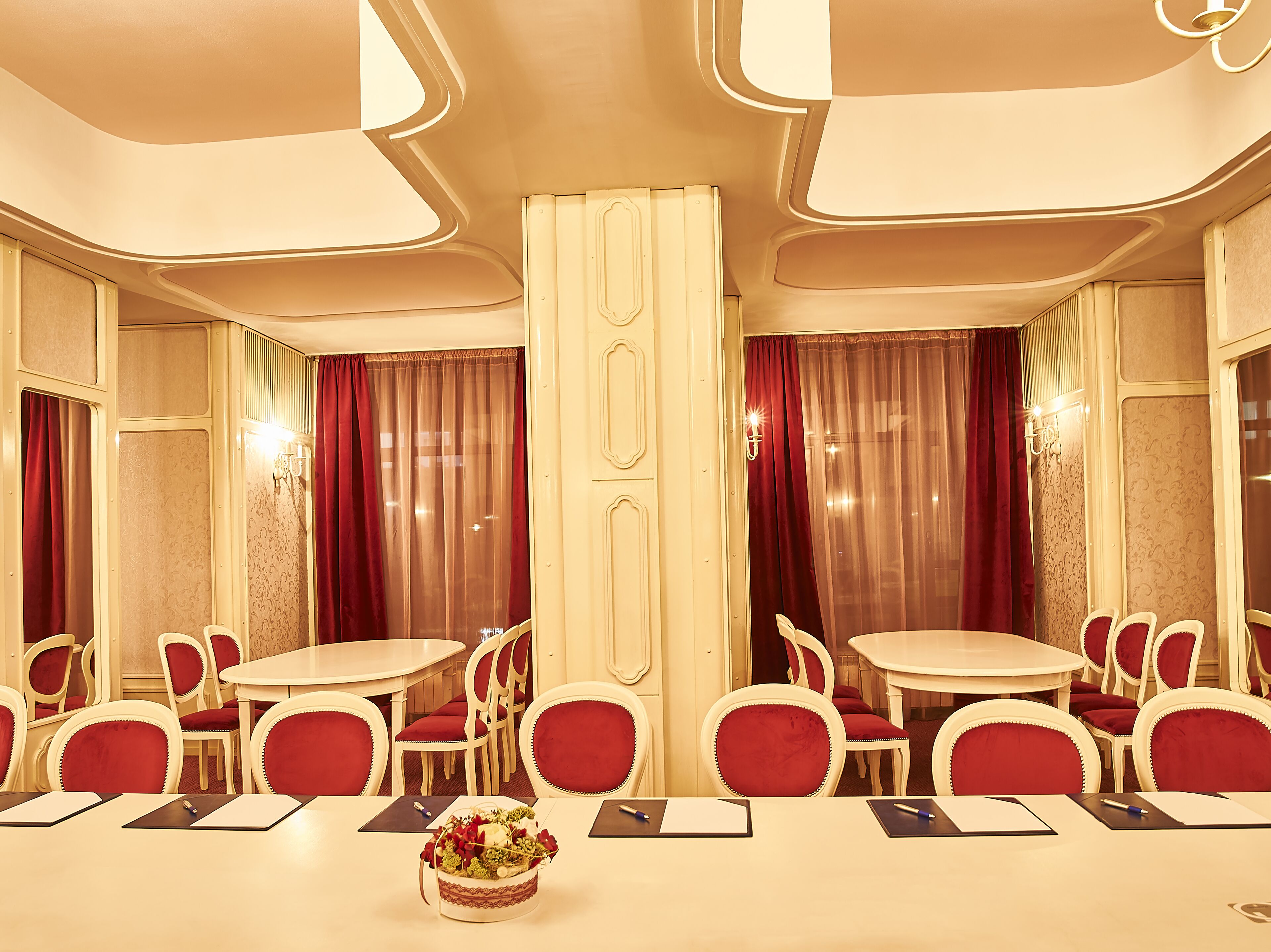 A hotel dining area with round tables, red upholstered chairs, and a floral centerpiece.