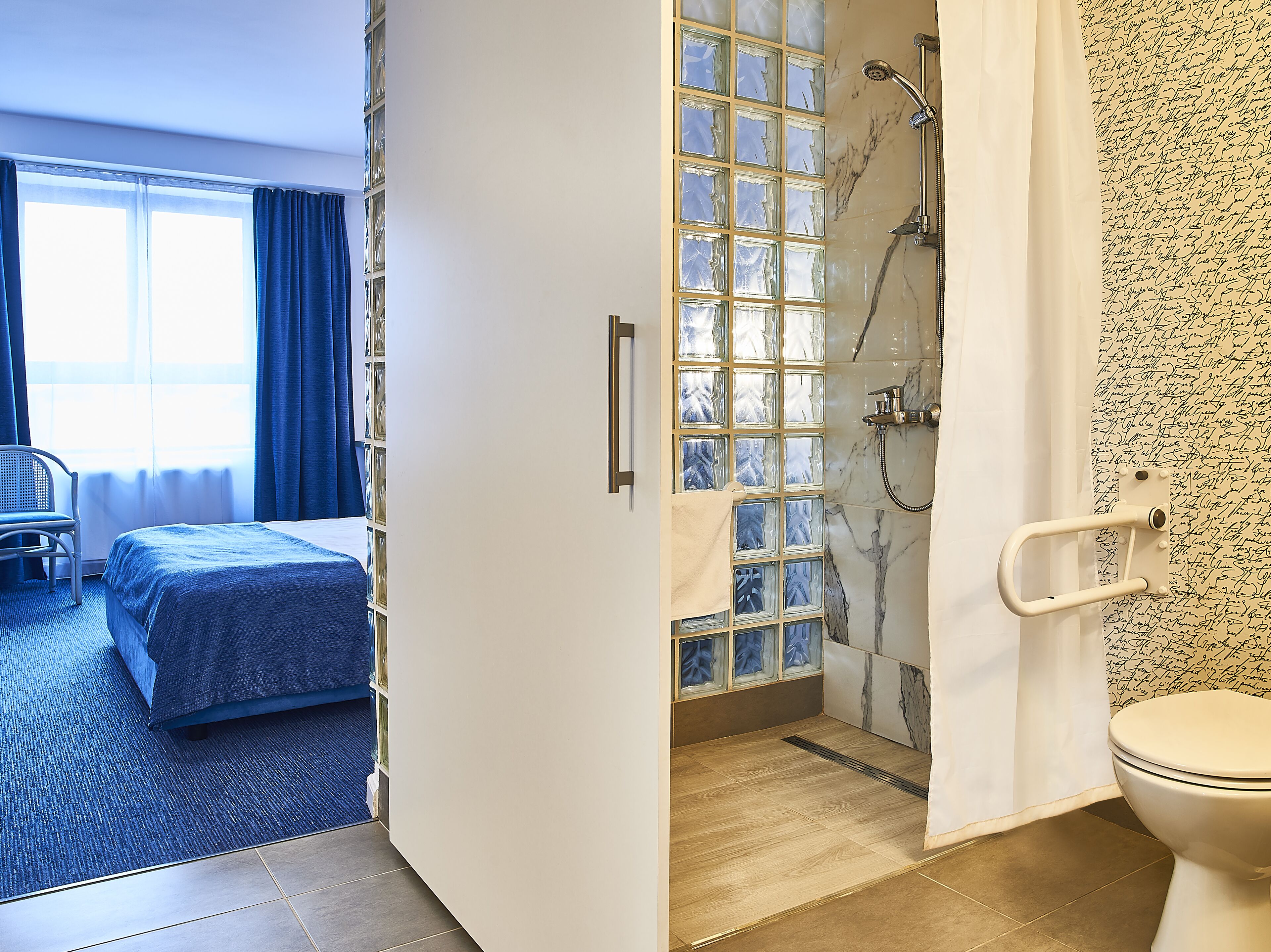 Une chambre d’hôtel comprenant un lit, une chaise, une douche avec des parois en verre et des toilettes.