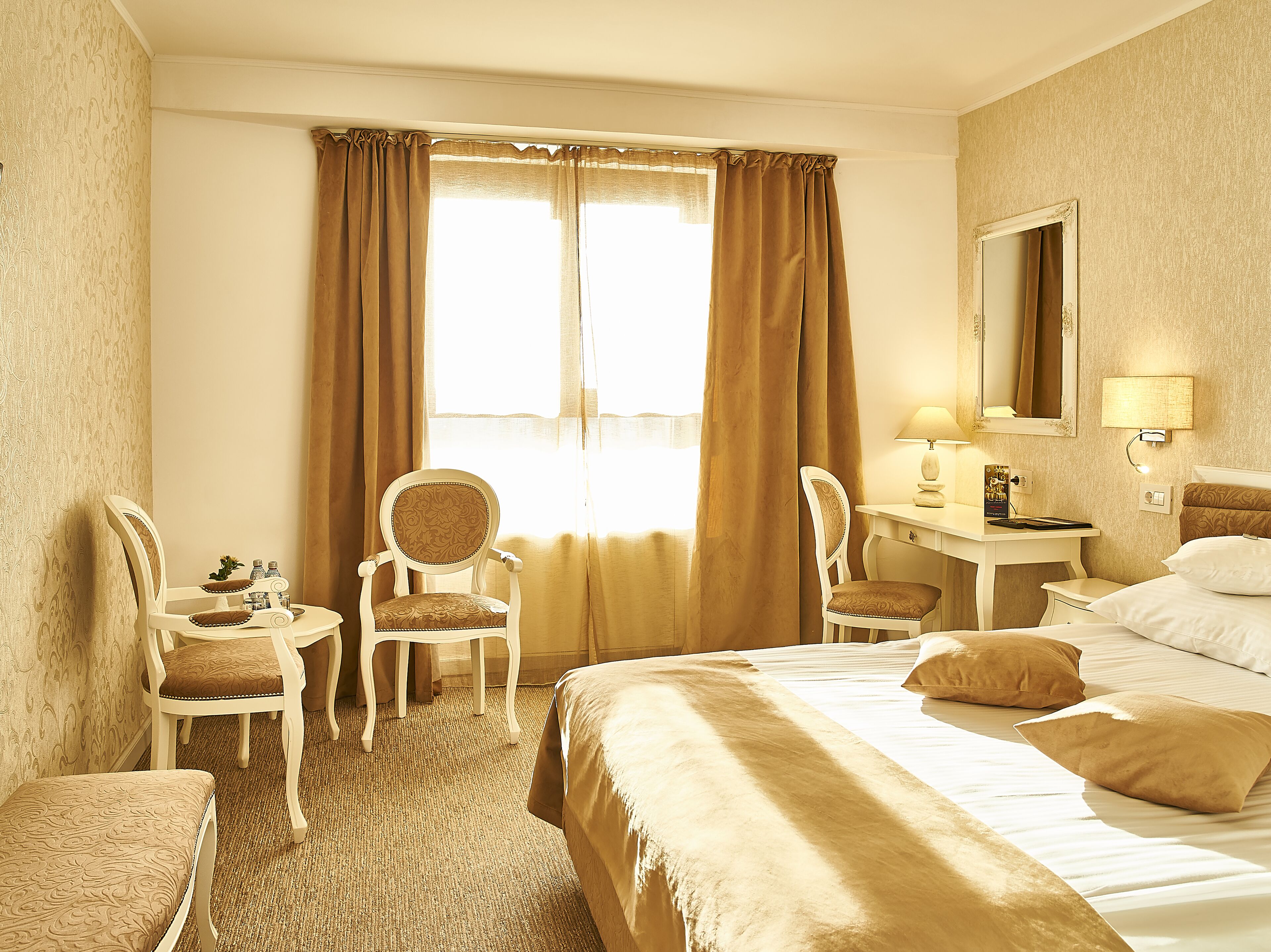 A hotel room with a large bed, two chairs, a desk, a lamp, and a mirror.