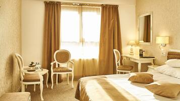 A hotel room with a large bed, two chairs, a desk, a lamp, and a mirror.