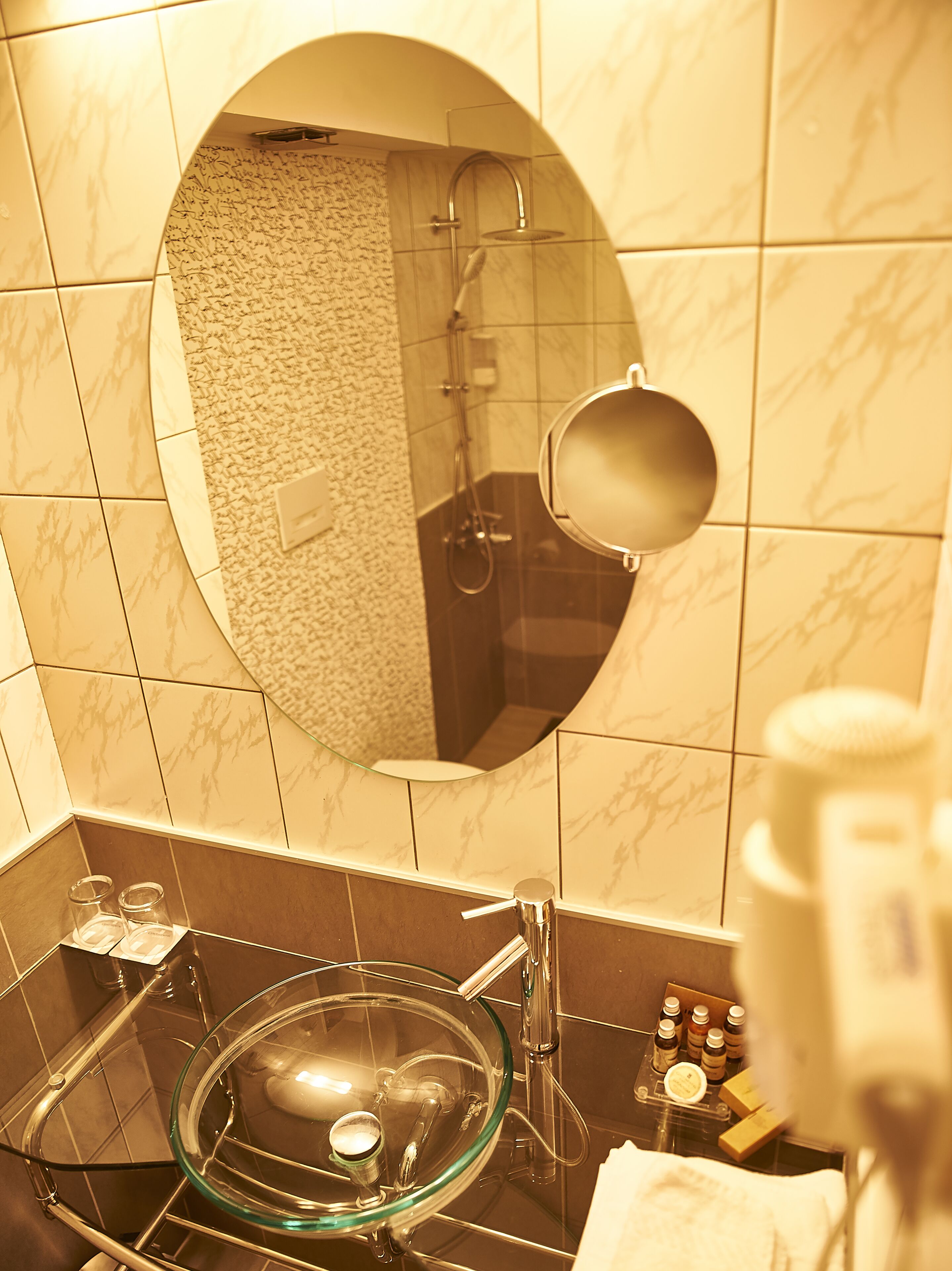 Een badkamer met een wastafel van glas, een handspiegel en toiletartikelen op het aanrecht.