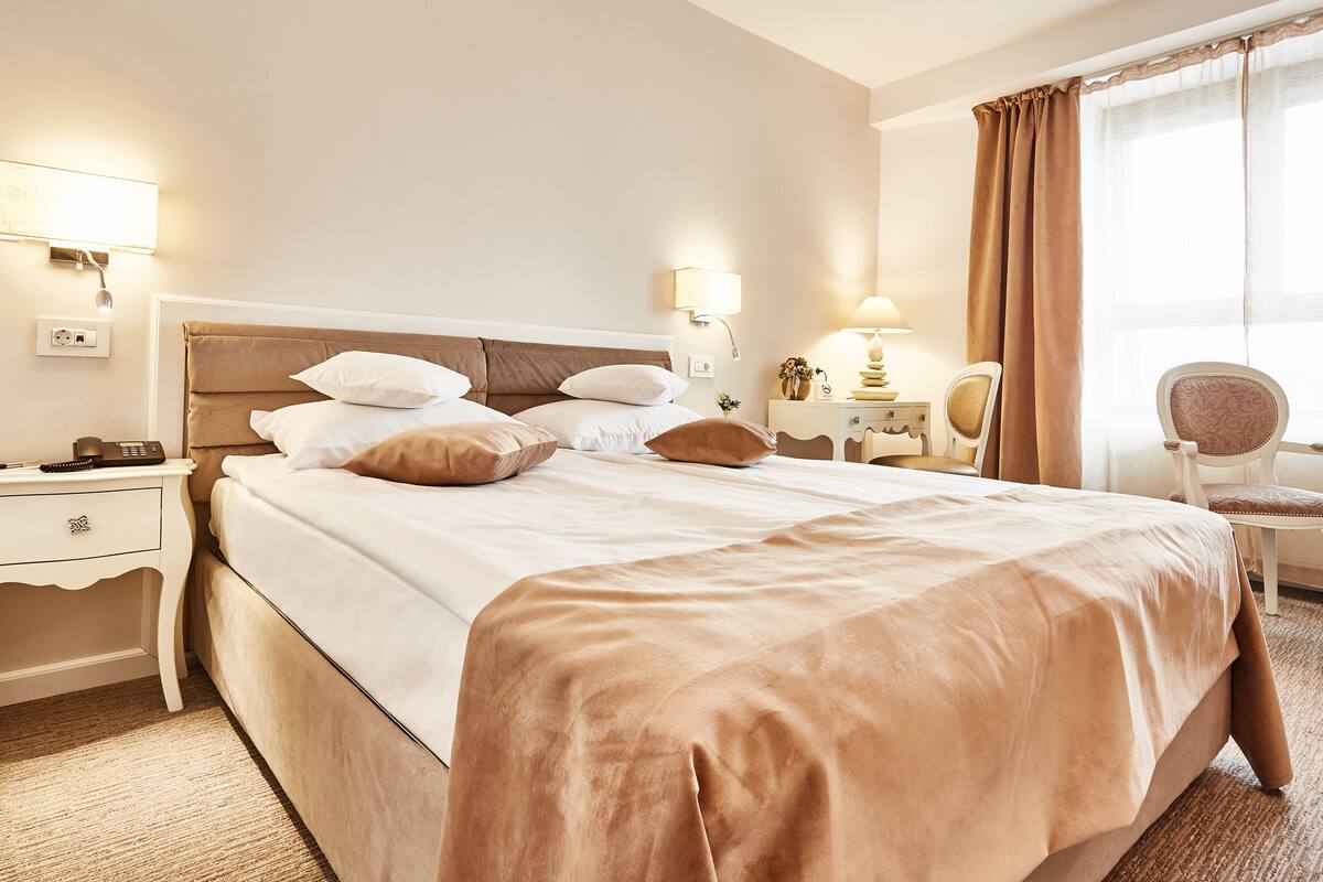 Ein Hotelzimmer mit einem großen Bett, Nachttischen, einem Sessel und einem Schreibtisch mit Lampe.