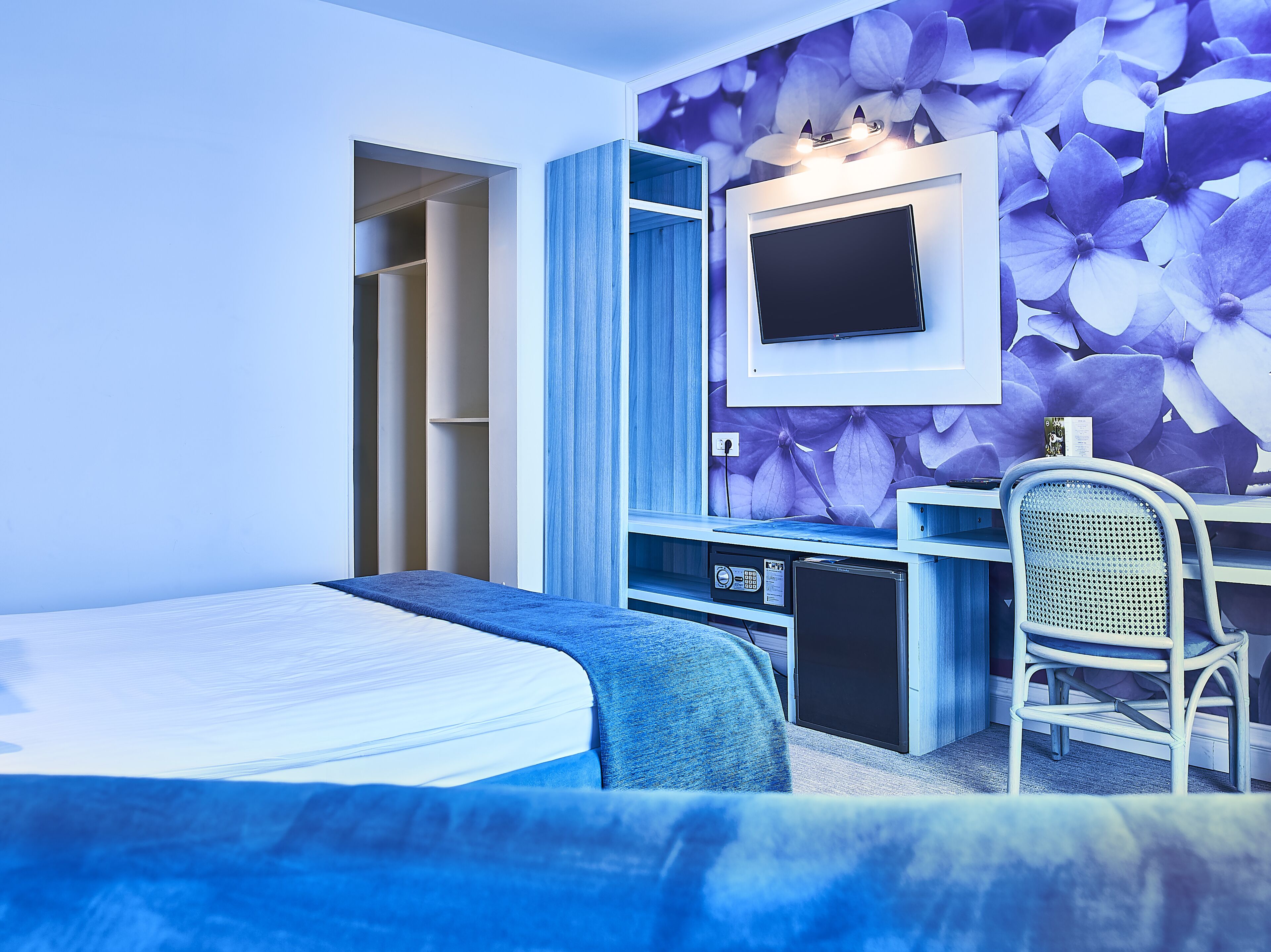 A bedroom with a bed, a desk with a chair, a TV, and a wardrobe.