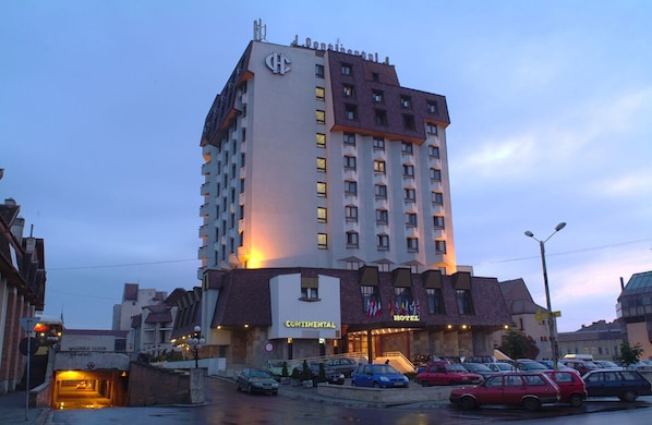A multi-story hotel with a prominent 'Continental' sign, a parking lot with several cars, and a clear sky. - Continental Forum Tirgu Mures (Targu Mures)