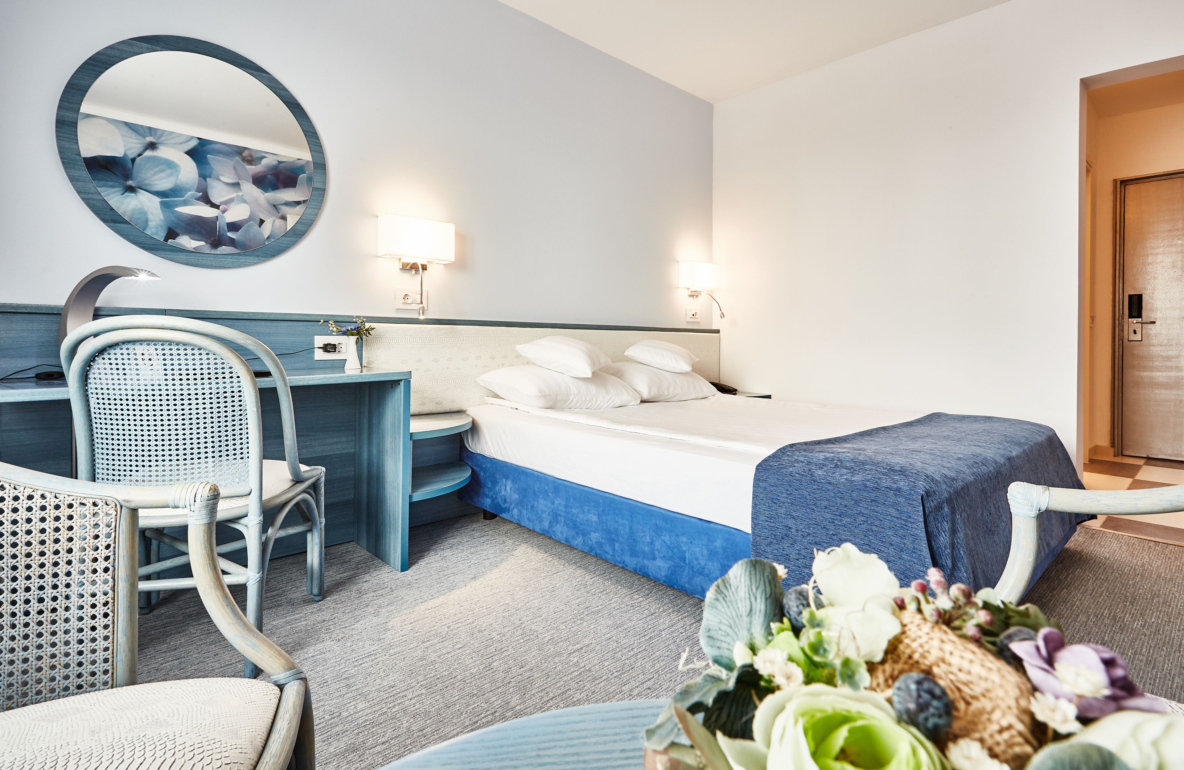 Ein Hotelzimmer mit einem Bett, einem Schreibtisch mit Stuhl, einem runden Spiegel und zwei Wandleuchten.