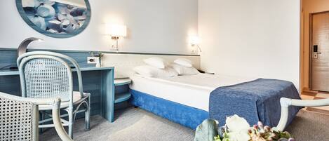 A hotel room with a bed, a desk with a chair, a round mirror, and two wall-mounted lamps.