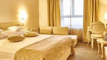A hotel room with a large bed, a chair, a small table, and a window with curtains.