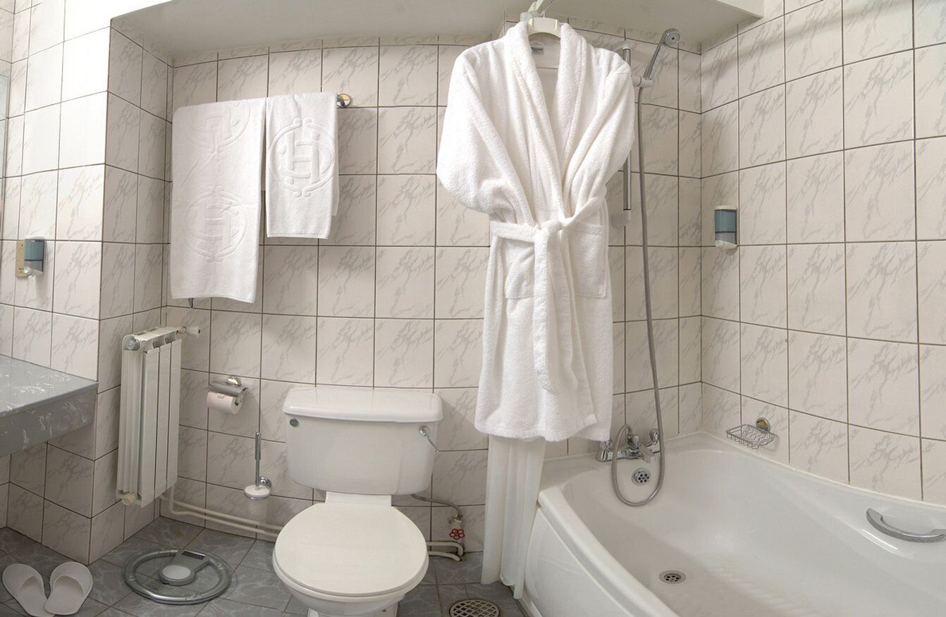 A bathroom with a toilet, bathtub, and a robe hanging on a rack.