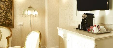 A hotel room with a white cabinet, a flat-screen TV mounted above it, a coffee maker, and two white cups on a tray.