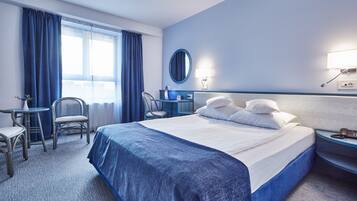 Habitación de hotel con una cama grande, un escritorio con silla, un espejo redondo y una mesita de noche con teléfono.
