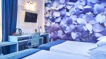A hotel room with a bed, a desk with a chair, a TV, and a wall with a floral wallpaper.