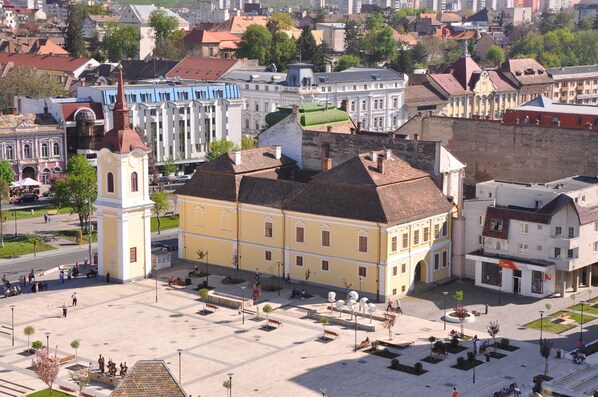 A spacious public square with a prominent yellow building featuring a clock tower, surrounded by other historic buildings and a clear sky. - Continental Forum Tirgu Mures (Targu Mures)