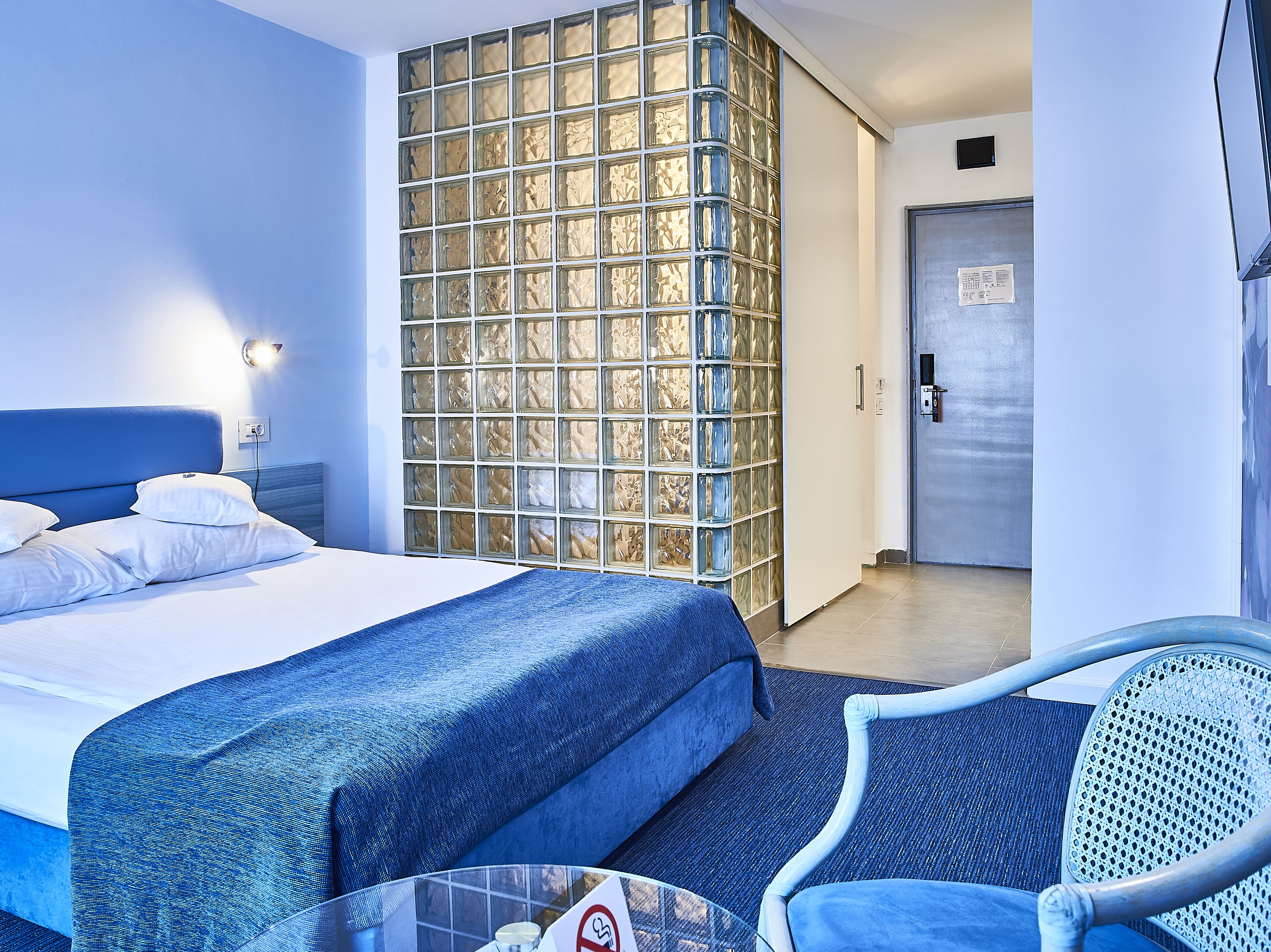 A hotel room with a bed, a seating area with a chair, and a wall with a patterned design.