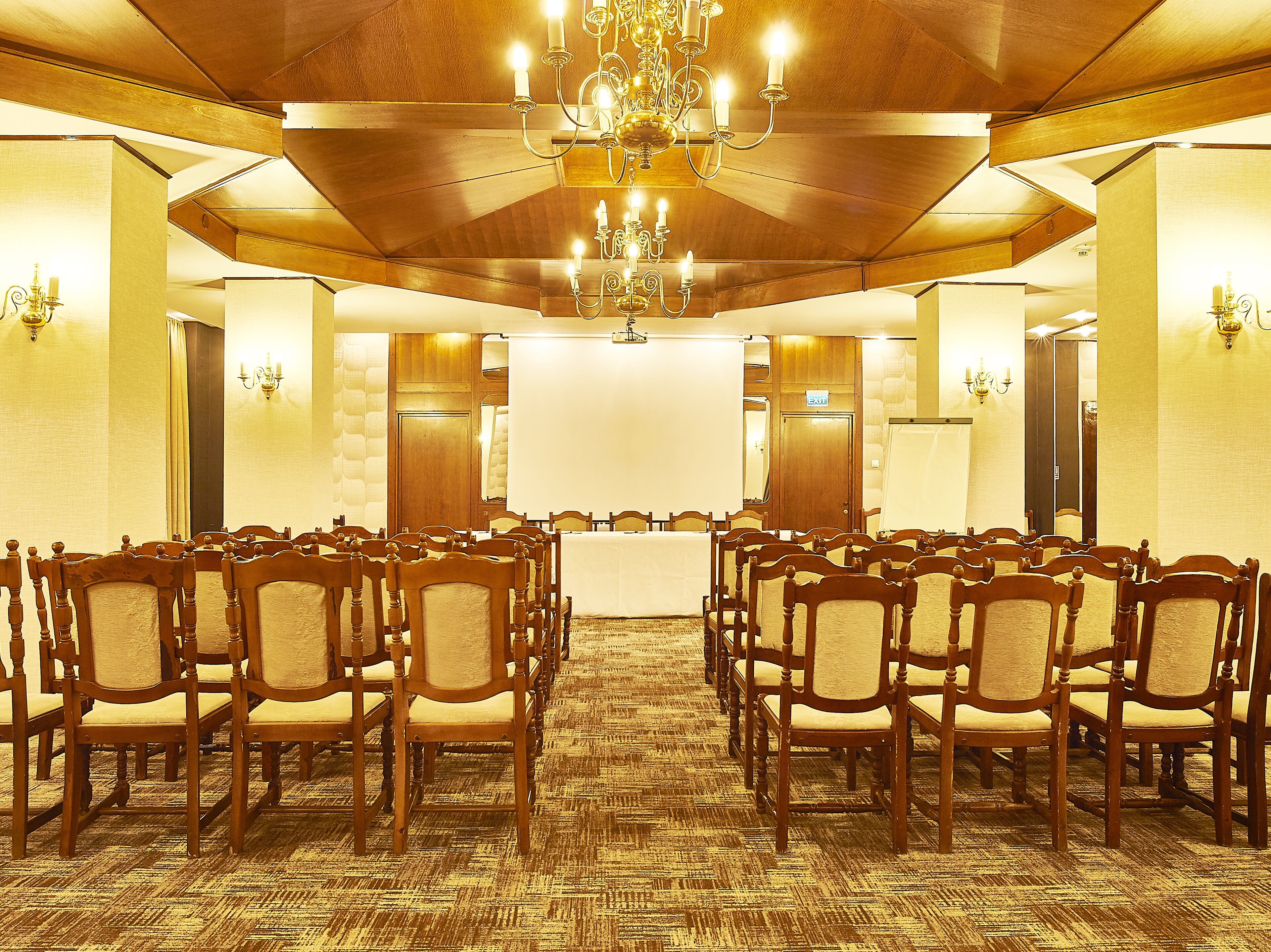A conference room with rows of wooden chairs, a large table, and a chandelier.