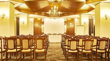 A conference room with rows of wooden chairs, a large table, and a chandelier.