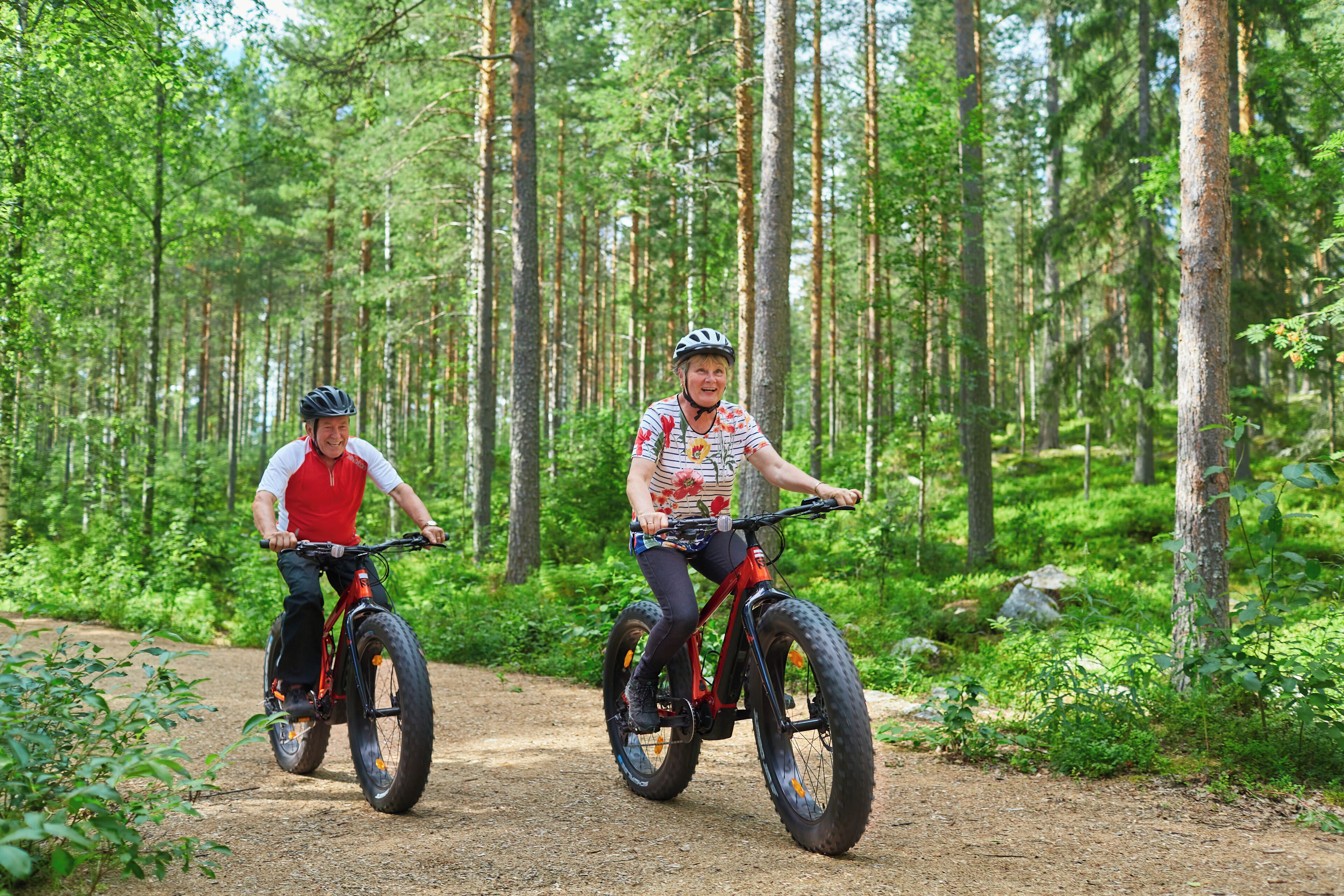 Dos personas pedaleando en bicicleta por un sendero de tierra en un bosque.