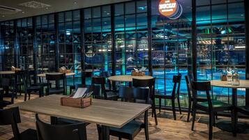 Een modern restaurant met uitzicht op het zwembad, met houten tafels en stoelen en een neonbord.