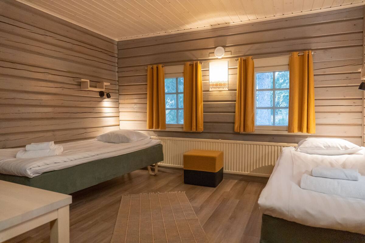 A room with two beds, a small table, and a window with curtains.