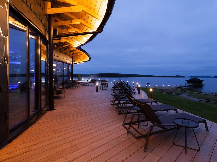 A wooden deck with outdoor seating and a view of a lake at dusk.
