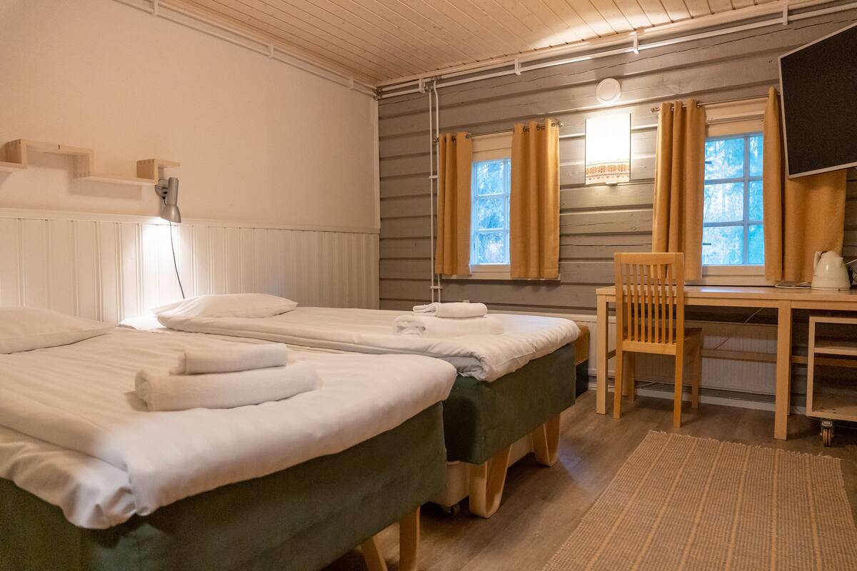 A room with two beds, a desk, a chair, and a window with curtains.