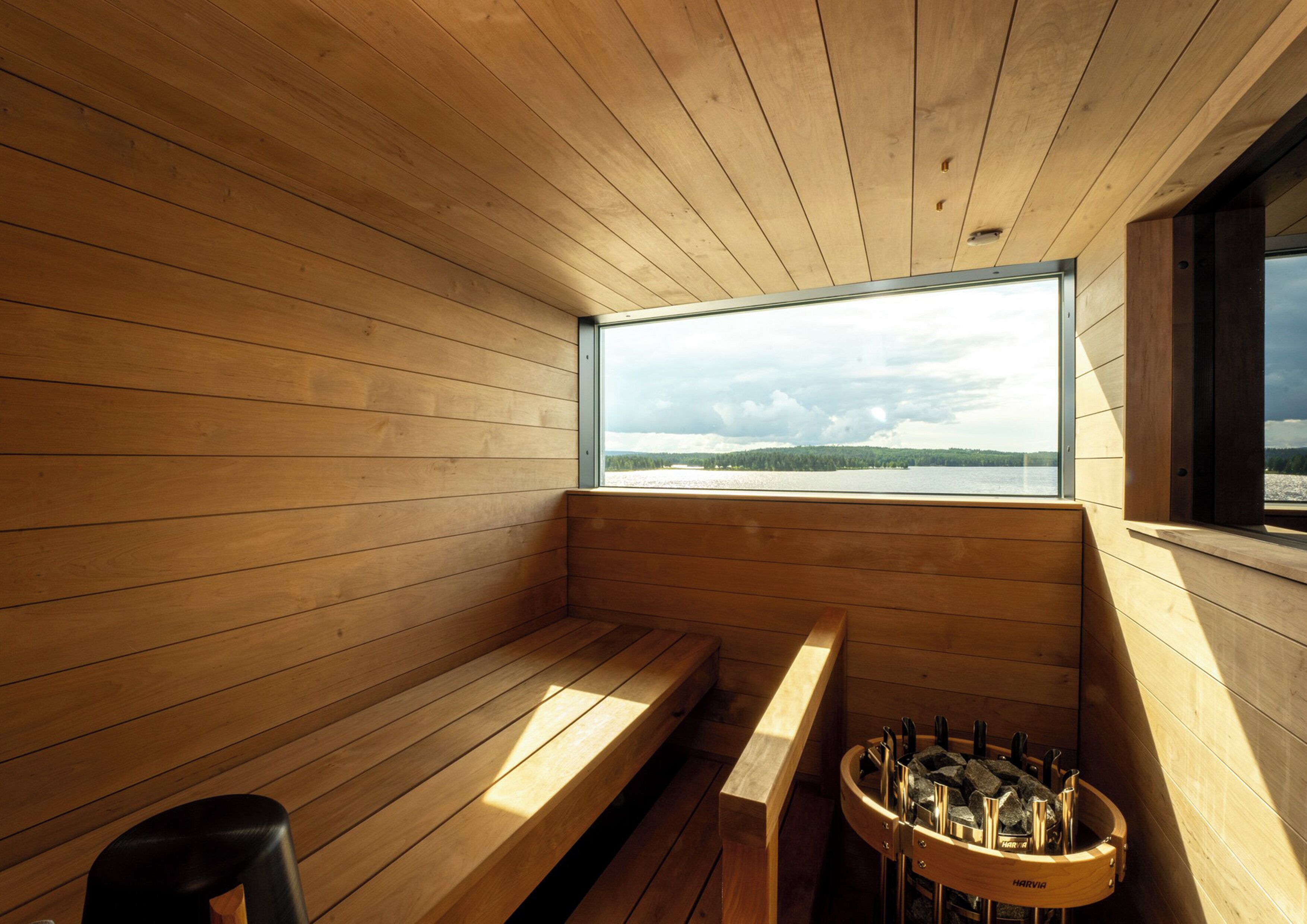 Ein Holzsaunaraum mit Bänken und einer Saunatisch, ein Fenster mit Seeblick und ein Saunatisch mit Flaschen.