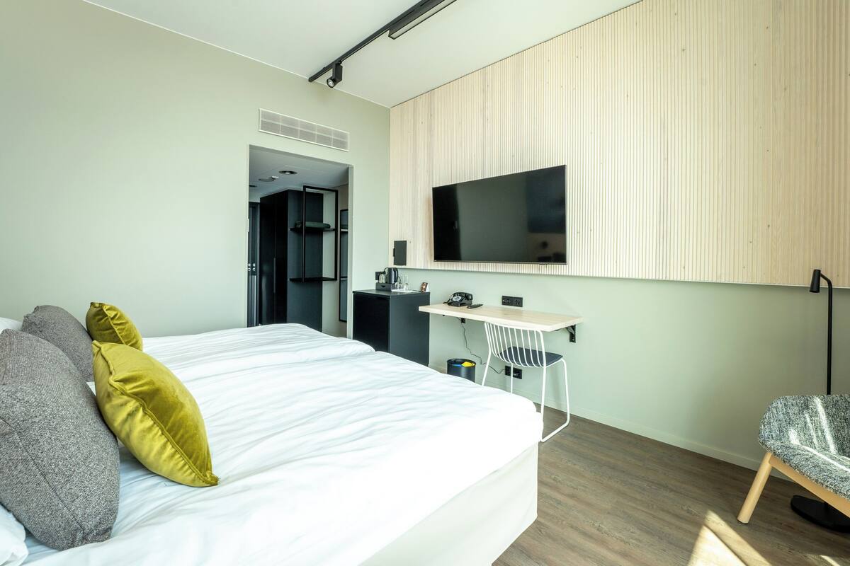 A modern hotel room with a large bed, a desk, and a TV mounted on the wall.