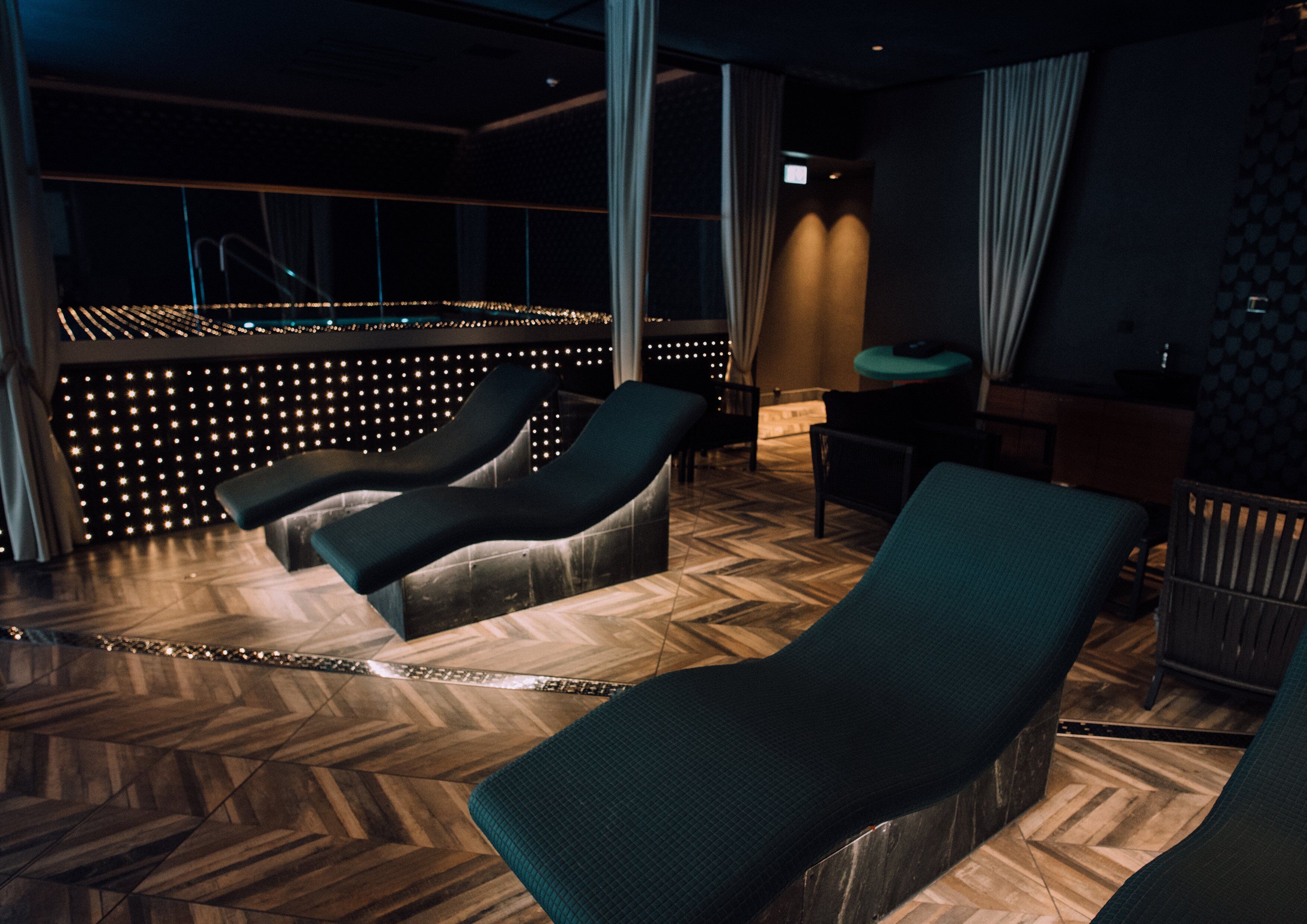 A spa room with massage chairs, a massage table, and a wall of lights.