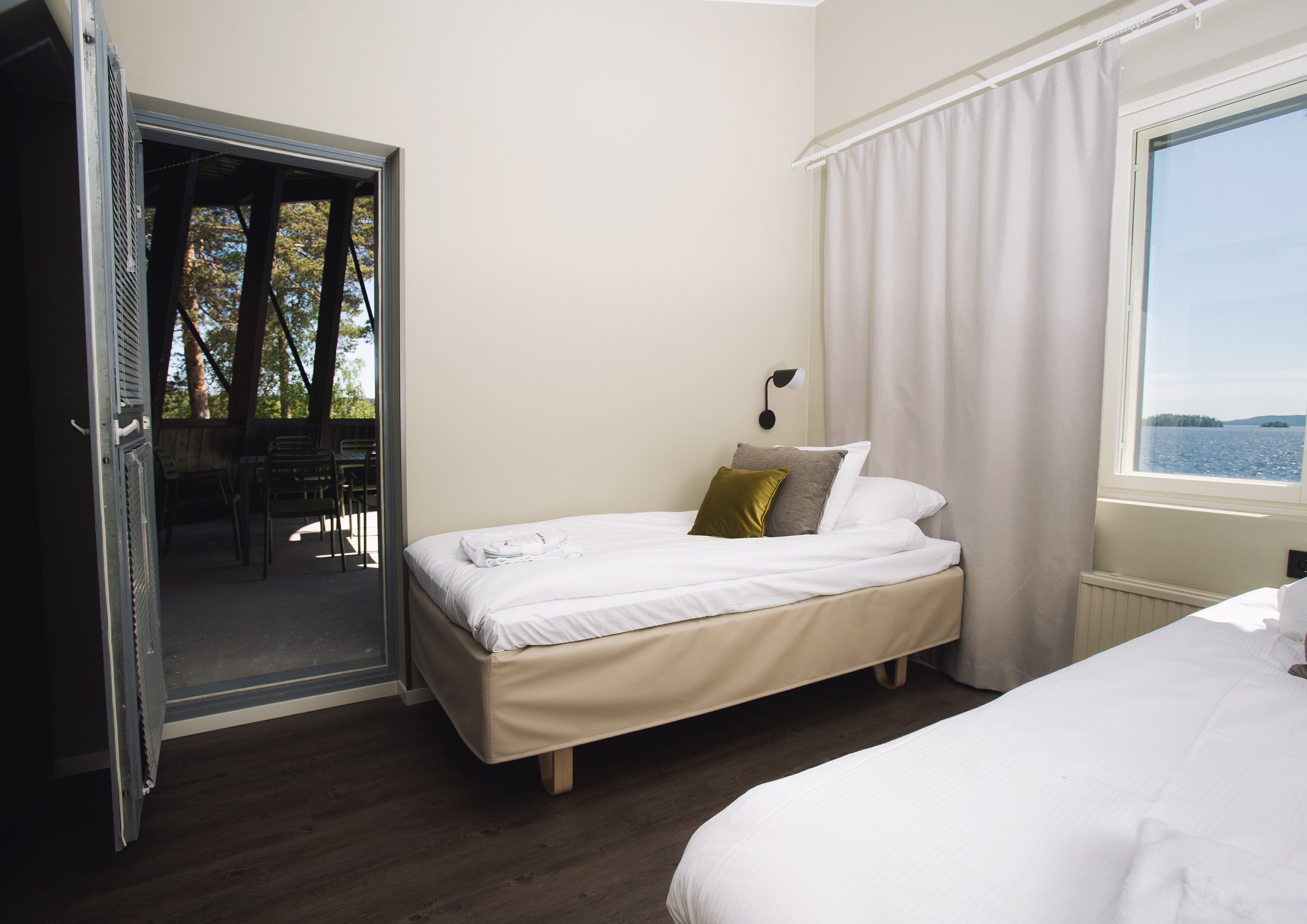 Une chambre avec un lit, une fenêtre donnant sur l’eau et une porte menant à un espace extérieur aménagé avec des chaises.
