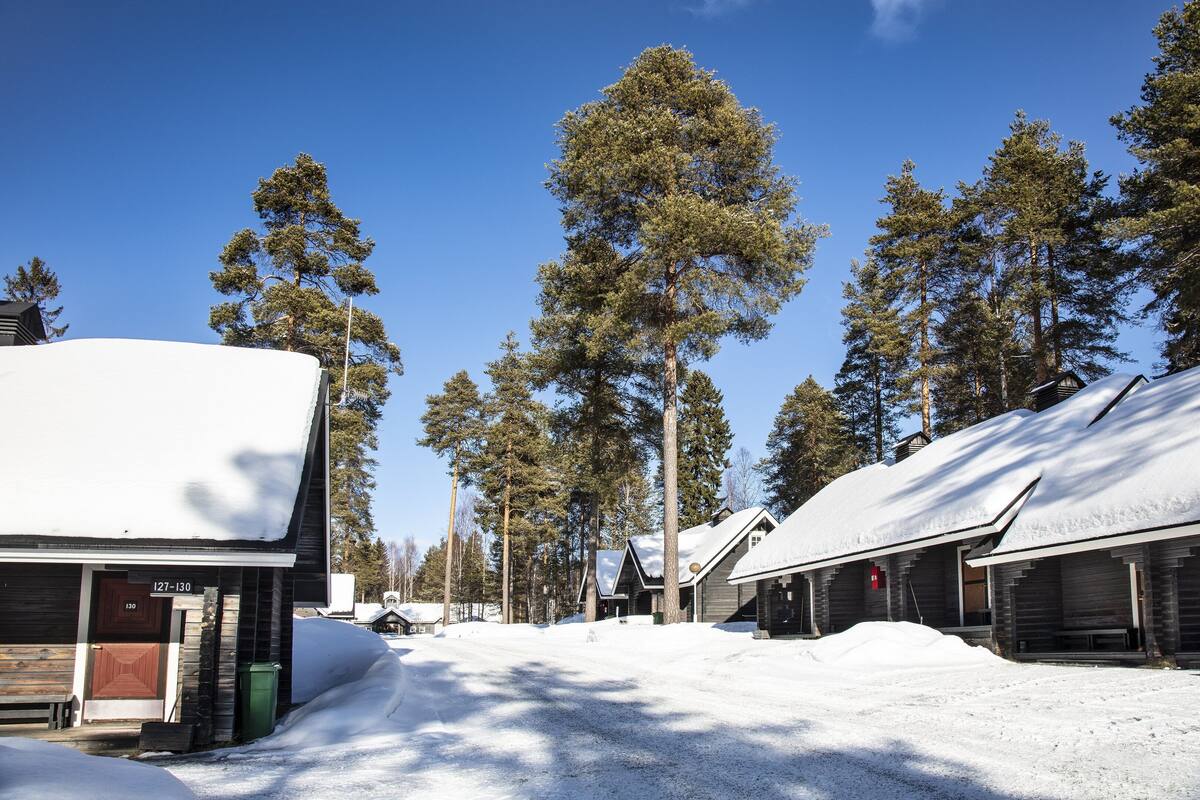 A snow-covered lodge with a wooden exterior, a red door, and a clear sky.