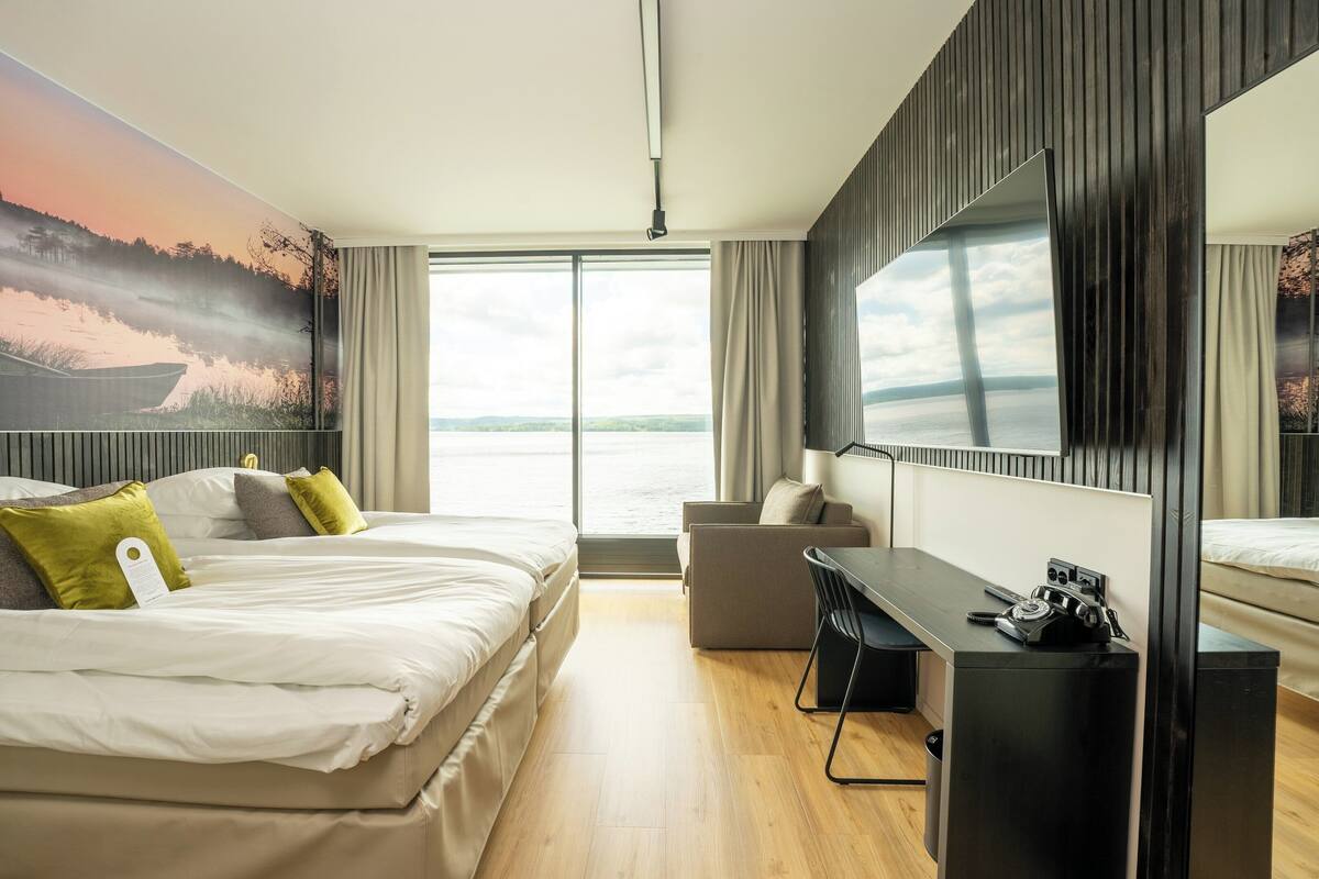 A modern hotel room with a large bed, a desk, and a view of the water.