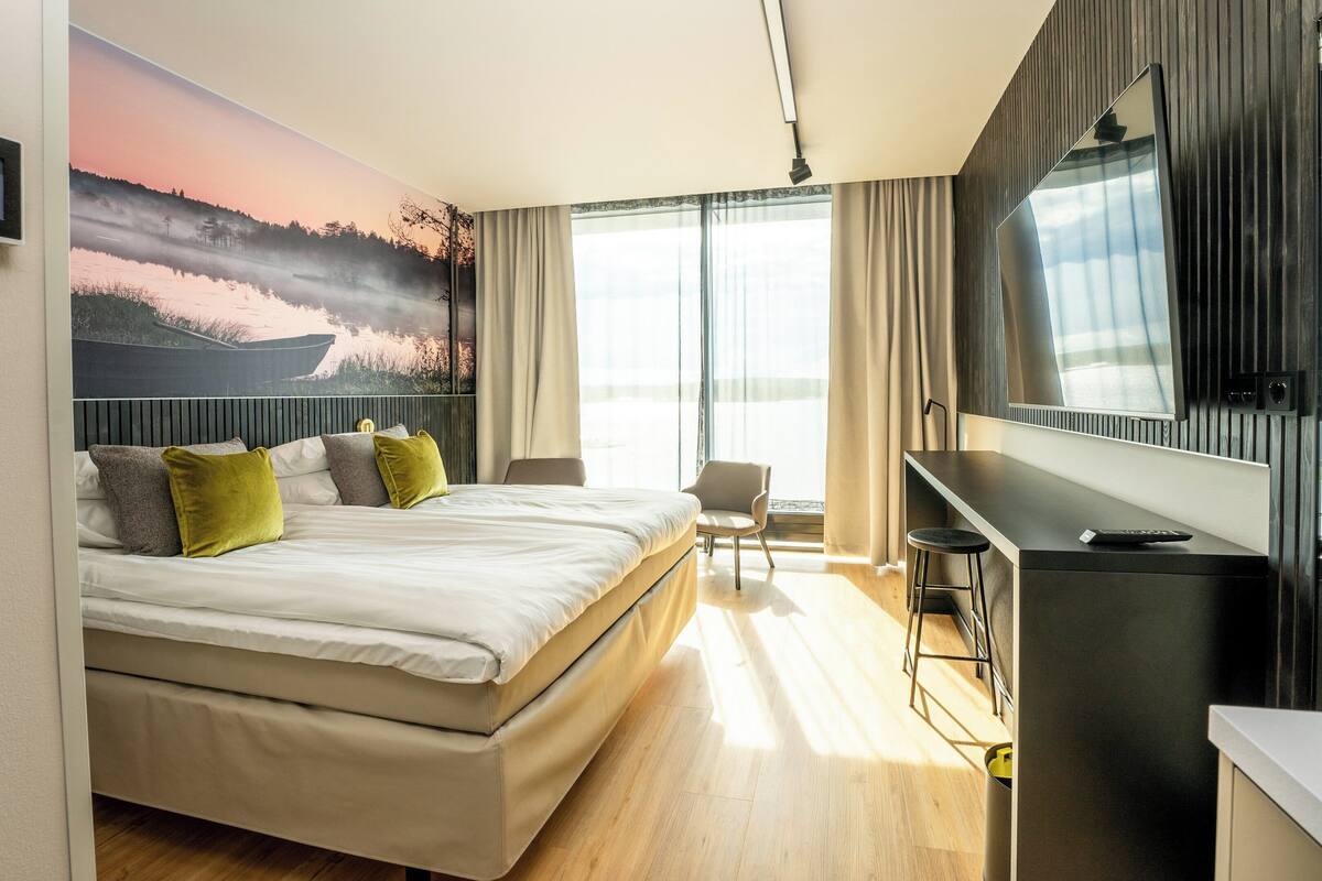 A modern hotel room with a large bed, a desk, and a TV.