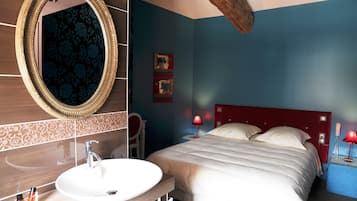 Habitación de hotel con un espejo ovalado grande, un lavamanos redondo, una cama con ropa de cama blanca, un cabecero rojo y dos lámparas de noche.