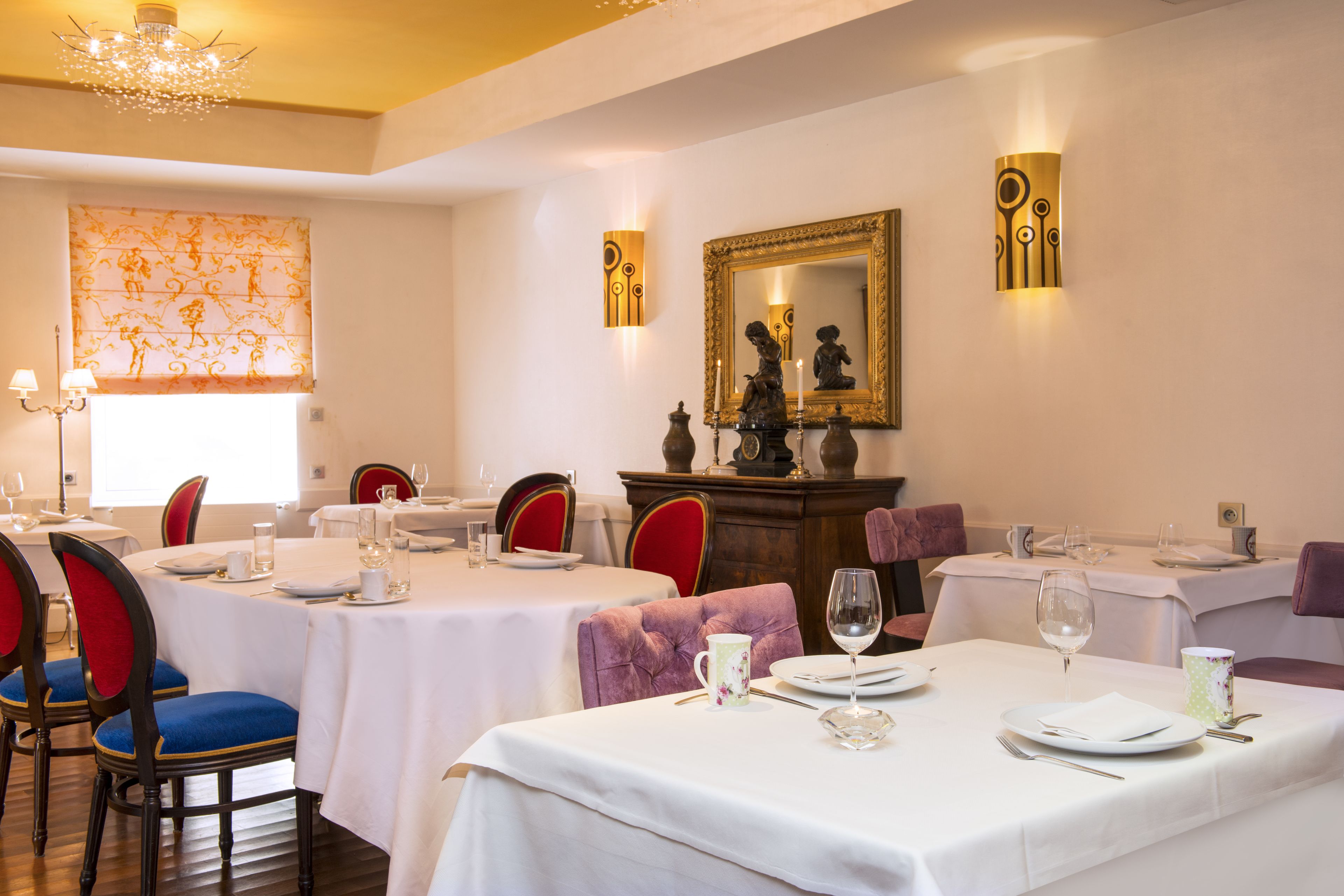 A dining area with tables set for service, chairs with cushioned seats, and a chandelier.