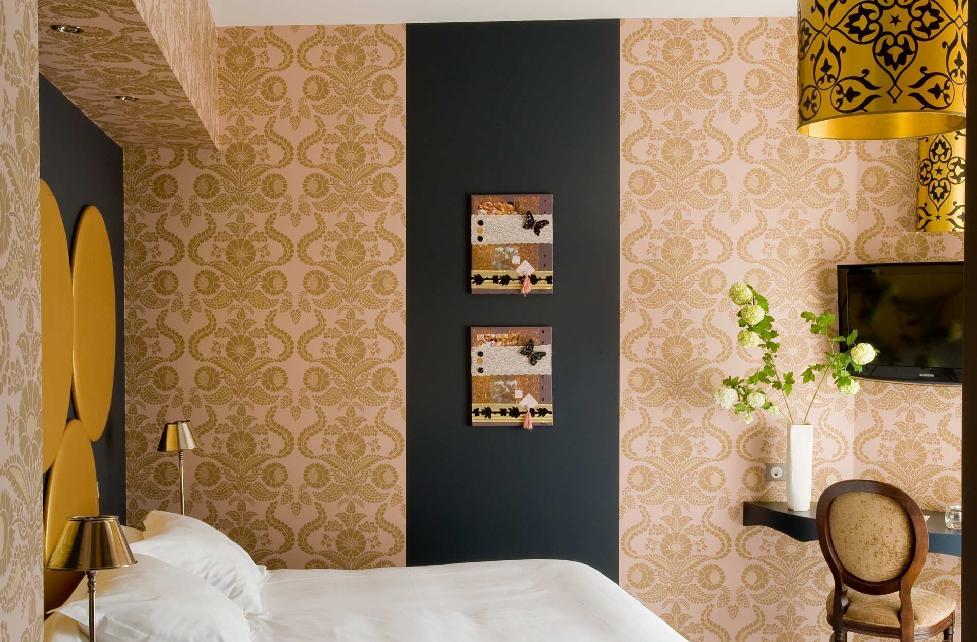 A hotel room with a bed, a desk with a chair, a television, and two wall-mounted artworks.