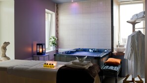 A spa room with a hot tub, a massage table, and a window with a view. - Carrion Cuisine Hôtel & Spa (Vire)