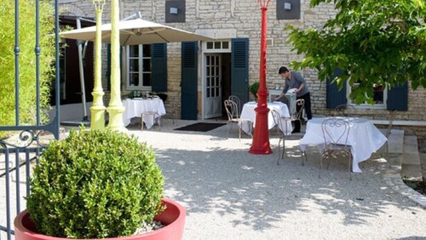 An outdoor dining area with tables and chairs, a red street lamp, and a stone building with shutters in the background. - Carrion Cuisine Hôtel & Spa (Vire)